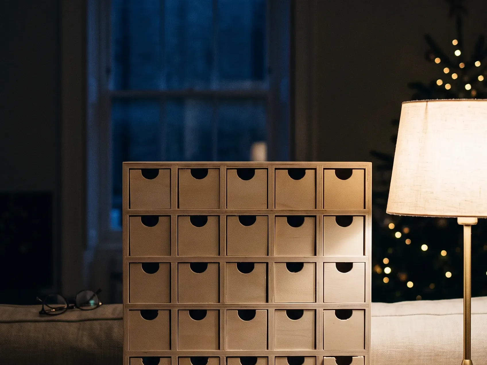 Wooden advent calendar with a grid of small drawers standing on a console beside a lit candle, Christmas decor ideas that mark the countdown